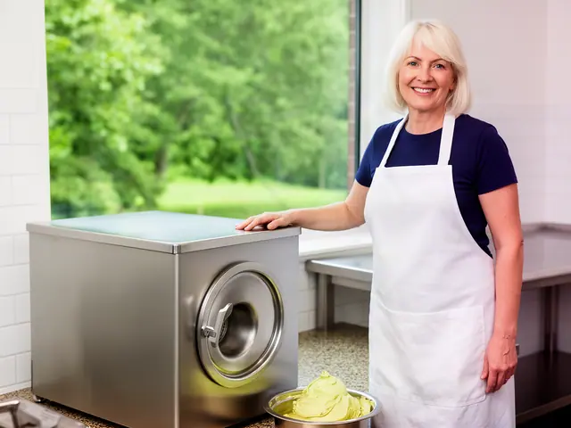 A smiling caterer in a white apron beside a new stainless-steel mixer with a bowl of buttercream.